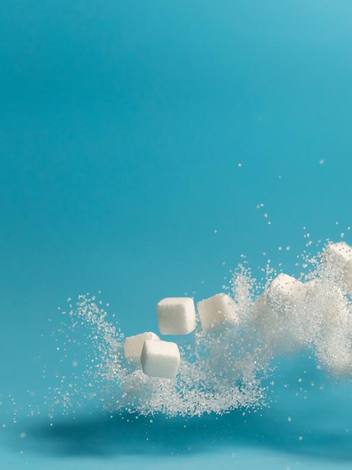 Fliegende und teilweise sich auflösende Zuckerstückchen vor blauem Hintergrund.
