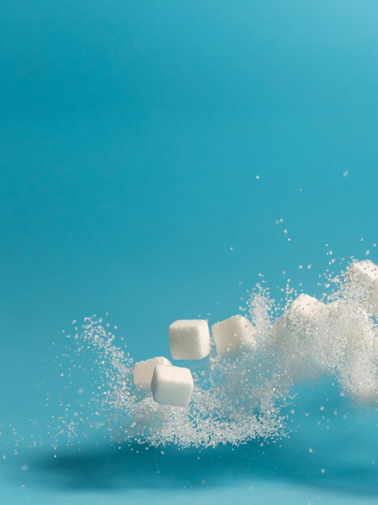 Fliegende und teilweise sich auflösende Zuckerstückchen vor blauem Hintergrund.