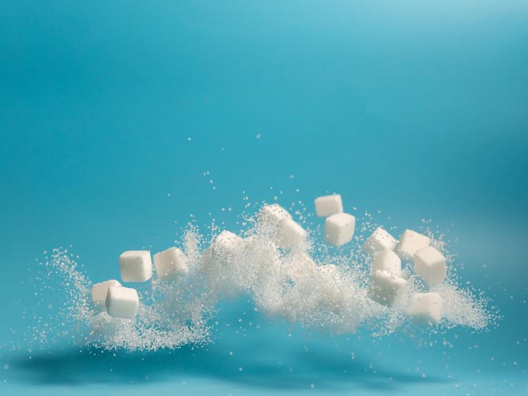 Fliegende und teilweise sich auflösende Zuckerstückchen vor blauem Hintergrund.