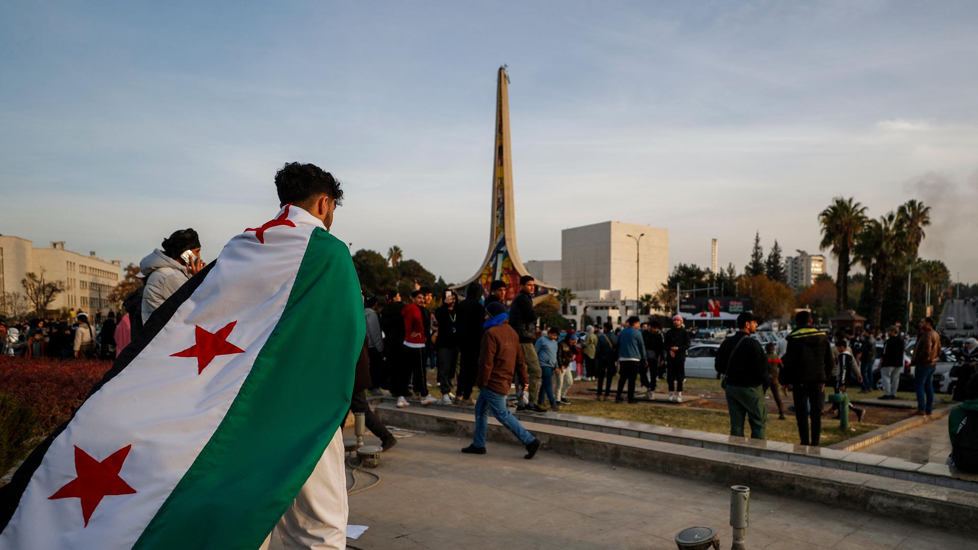 Ein Mann mit Revolutionsflagge auf dem Rücken geht über einen Platz in Damaskus, Syrien.