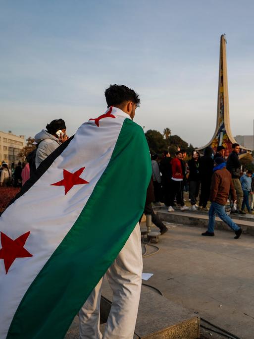 Ein Mann mit Revolutionsflagge auf dem Rücken geht über einen Platz in Damaskus, Syrien.