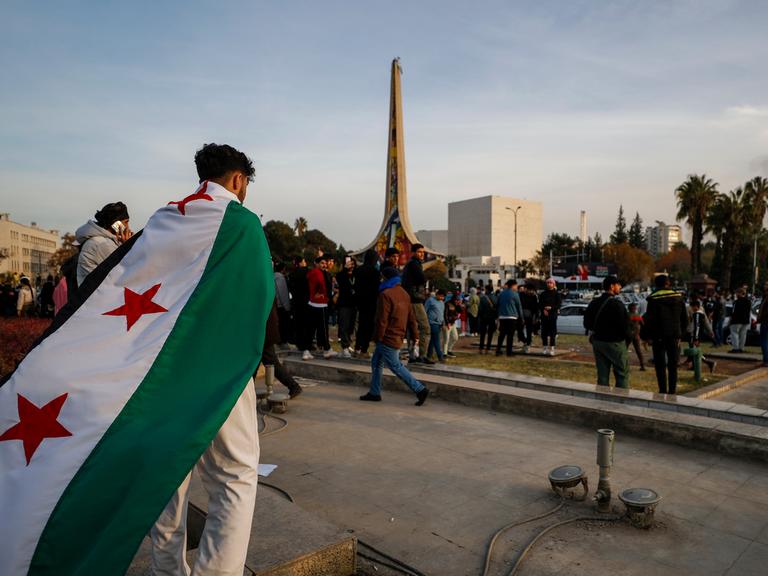 Ein Mann mit Revolutionsflagge auf dem Rücken geht über einen Platz in Damaskus, Syrien.