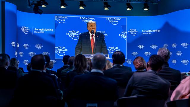 US-Präsident Donald Trump ist auf einer Großbildleinwand zu sehen, während er eine Rede hält. Im Vordergrund einige Zuhörerinnen und Zuhörer.