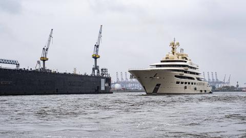 Eine weiße Yacht fährt durch den Hamburger Hafen neben Kränen.