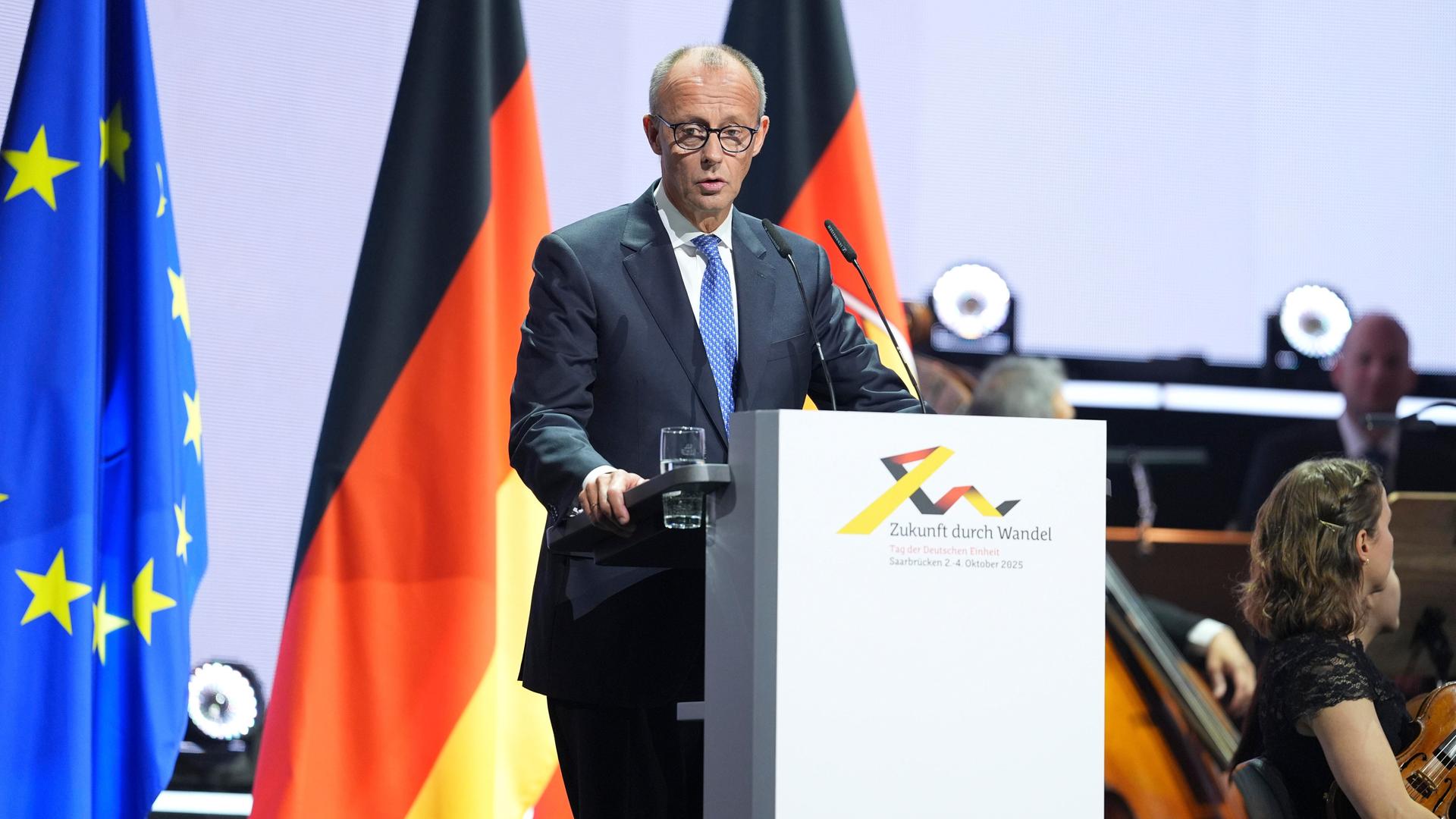 Bundeskanzler Friedrich Merz steht am Rednerpult. Im Hintergrund die Flagge Deutschlands und die der Europäischen Union.