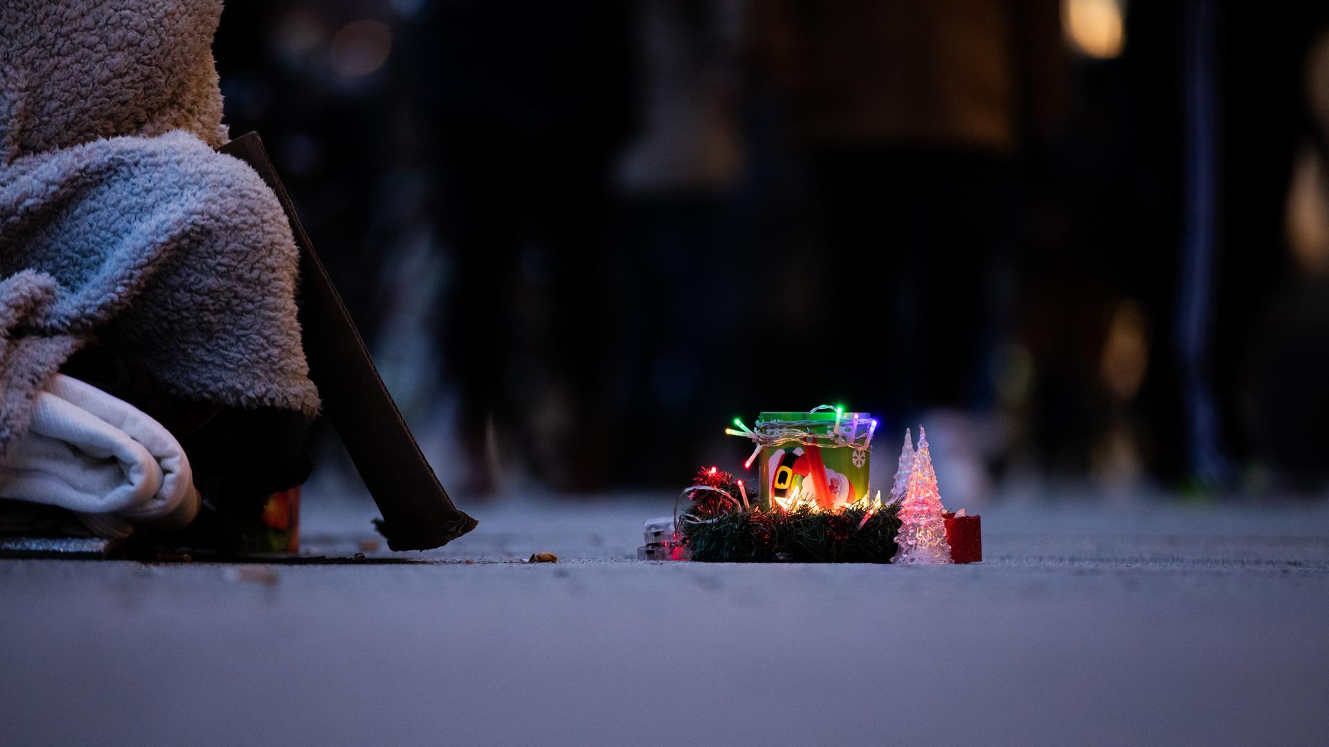 Ein Obdachloser bittet mit einer weihnachtlich gestalteten Spendendose um Geld.