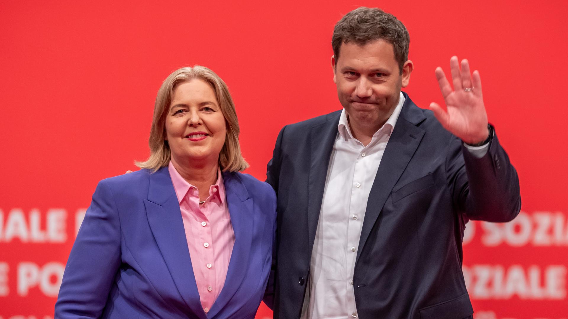 Die beiden winken lächelnd in die Kamera. Hinter ihnen eine rote Wand mit weißen SPD-Schriftzügen. Die beiden winken lächelnd in die Kamera. Hinter ihnen eine rote Wand mit weißen SPD-Schriftzügen.