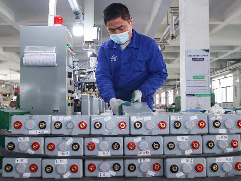 Ein Arbeiter in einem Blaumann stapelt Batterien in einer Fabrik in China.
