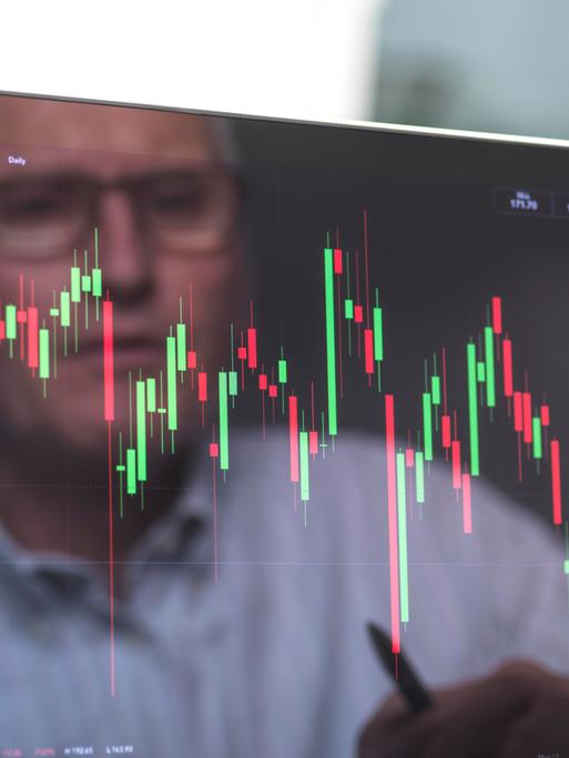 Börsianer spiegelt sich in einem Bildschirm, der mann betrachtet die Grafik eines Börsenkurses