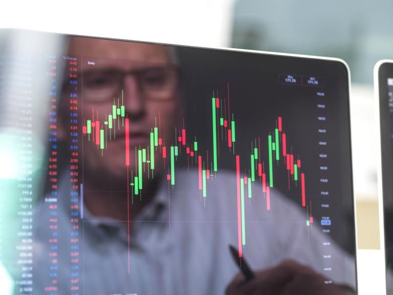 Börsianer spiegelt sich in einem Bildschirm, der mann betrachtet die Grafik eines Börsenkurses