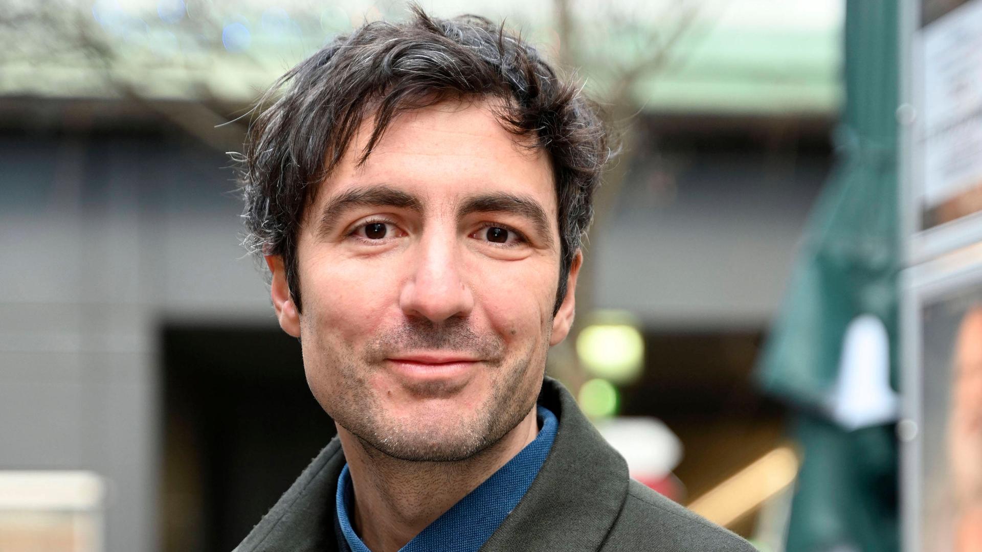 İlker Çatak trägt einen grauen Mantel und posiert im Freien für ein Porträt.