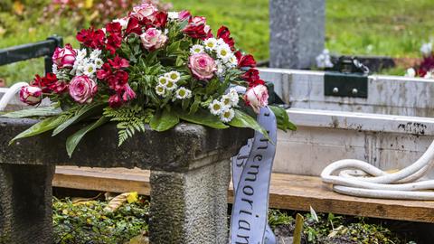 Ein Trauerkranz liegt kurz vor der Beerdigung einer verstorbenen Person vor einen offenen Grab.