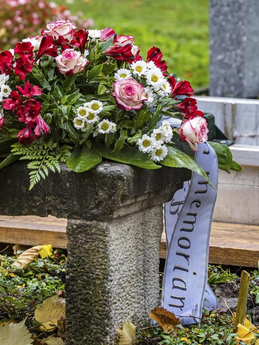 Ein Trauerkranz liegt kurz vor der Beerdigung einer verstorbenen Person vor einen offenen Grab.