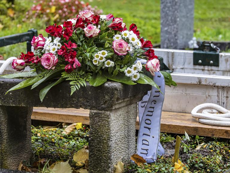 Ein Trauerkranz liegt kurz vor der Beerdigung einer verstorbenen Person vor einen offenen Grab.