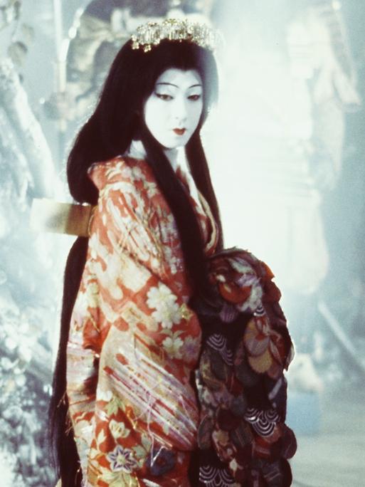 Eine weiß geschminkte japanische Frau in traditionellem Kostüm in einer fantasy-artig anmutenden Umgebung