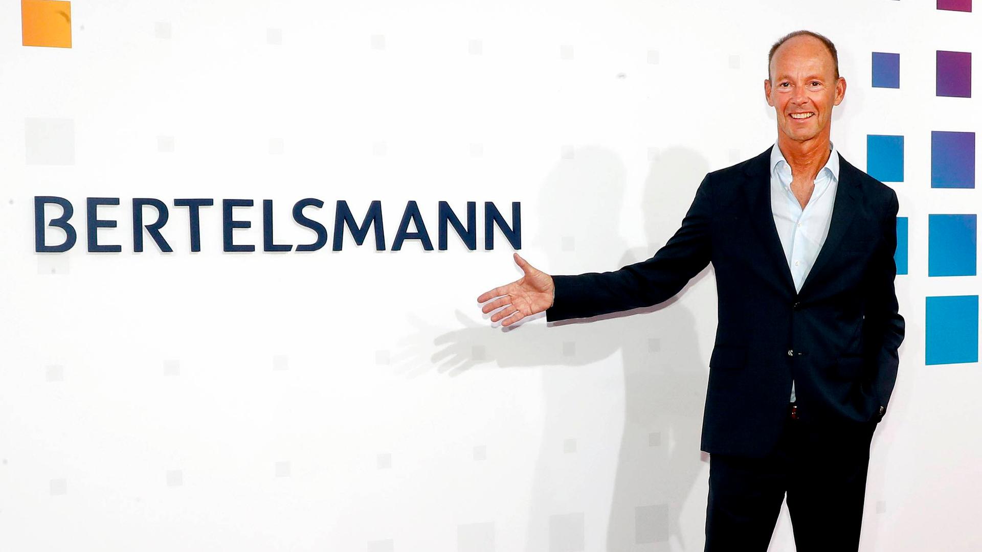 Der Vorstandsvorsitzende von Bertelsmann Thomas Rabe zeigt mit der Hand auf das Firmenlogo.