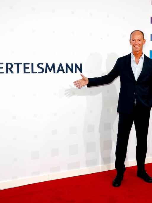 Der Vorstandsvorsitzende von Bertelsmann Thomas Rabe zeigt mit der Hand auf das Firmenlogo.