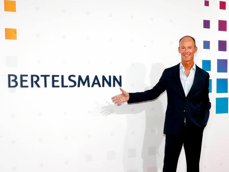 Der Vorstandsvorsitzende von Bertelsmann Thomas Rabe zeigt mit der Hand auf das Firmenlogo.