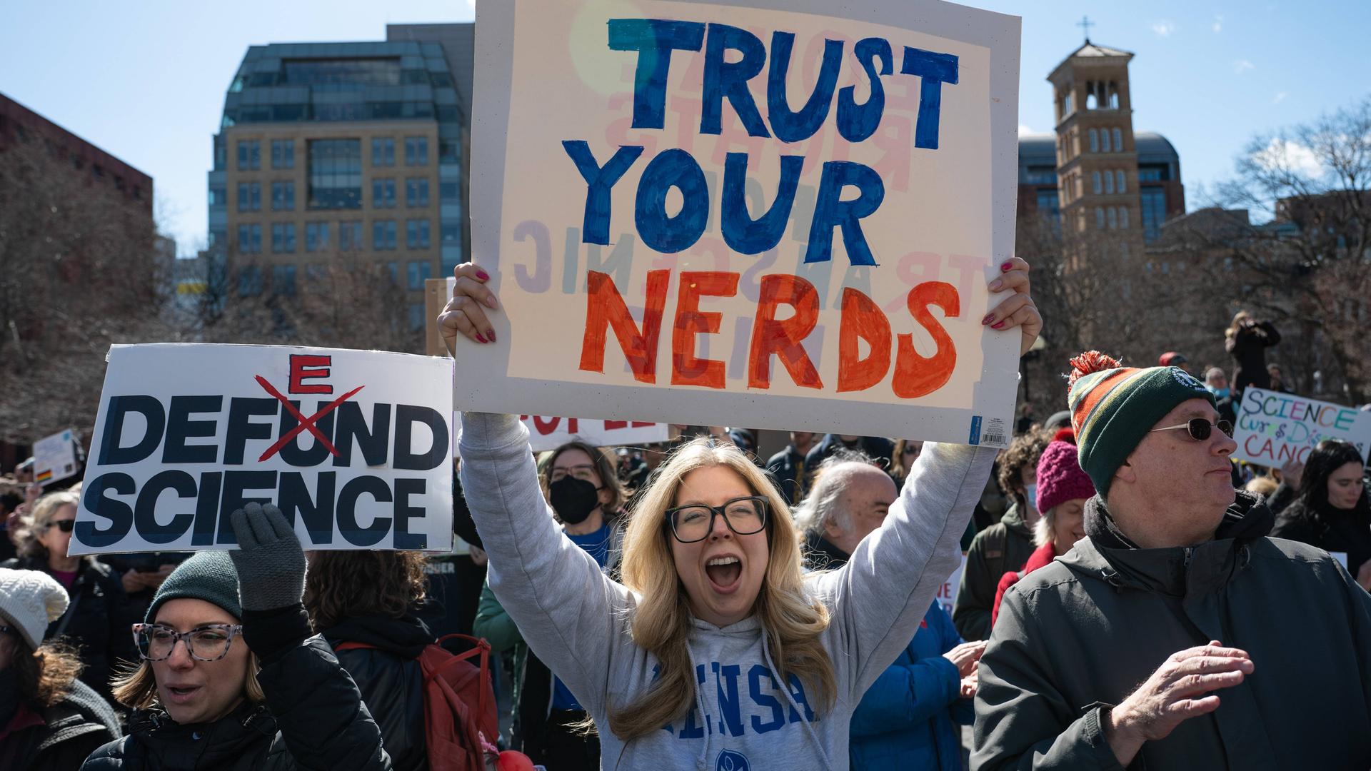 Menschen auf einer Demonstration, im Vordergrund steht eine Frau und hält ein Schild mit der Aufschrift "Trust Your Nerds"
