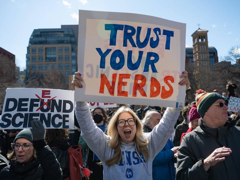 Menschen auf einer Demonstration, im Vordergrund steht eine Frau und hält ein Schild mit der Aufschrift "Trust Your Nerds" Menschen auf einer Demonstration, im Vordergrund steht eine Frau und hält ein Schild mit der Aufschrift "Trust Your Nerds"