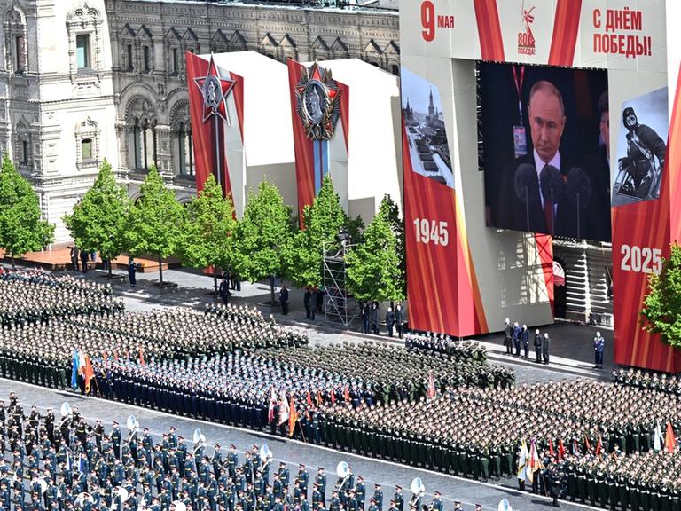 Unzähliche Soldaten marschieren, darüber zeigt eine große Videoleinwand Putin: Militärparade zum 80. Jahrestag des Sieges über Nazideutschland in Moskau.