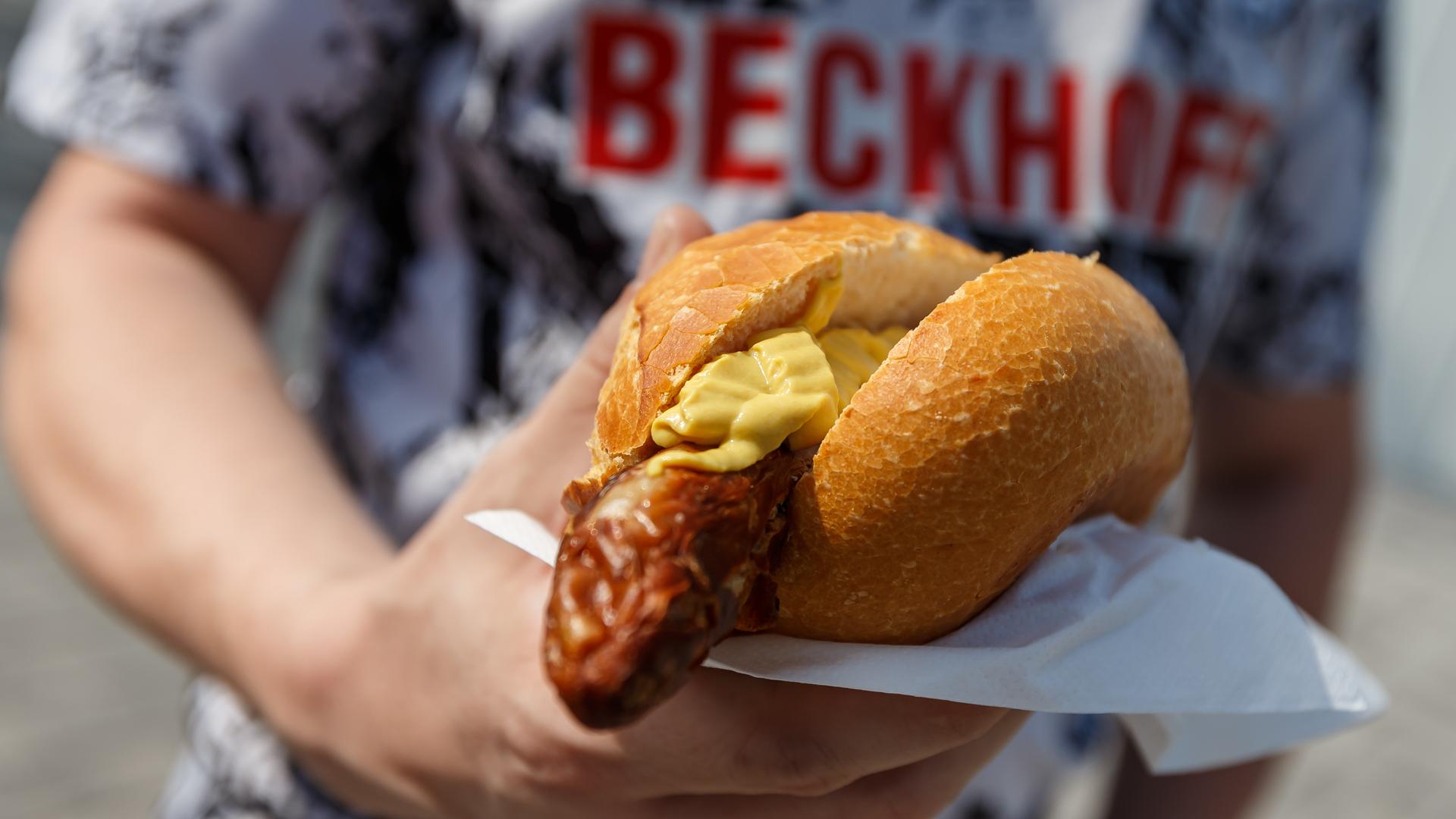 Bratwurst mit Senf im Brötchen, gehalten von einem Fan des SC Verl beim Spiel gegen den SV Waldhof Mannheim 