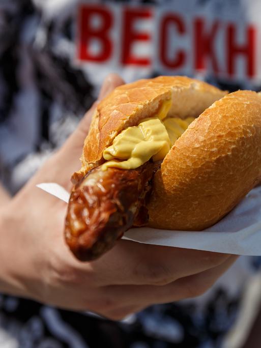 Bratwurst mit Senf im Brötchen, gehalten von einem Fan des SC Verl beim Spiel gegen den SV Waldhof Mannheim 