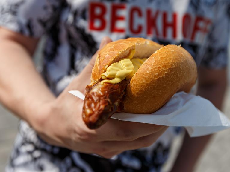 Bratwurst mit Senf im Brötchen, gehalten von einem Fan des SC Verl beim Spiel gegen den SV Waldhof Mannheim 