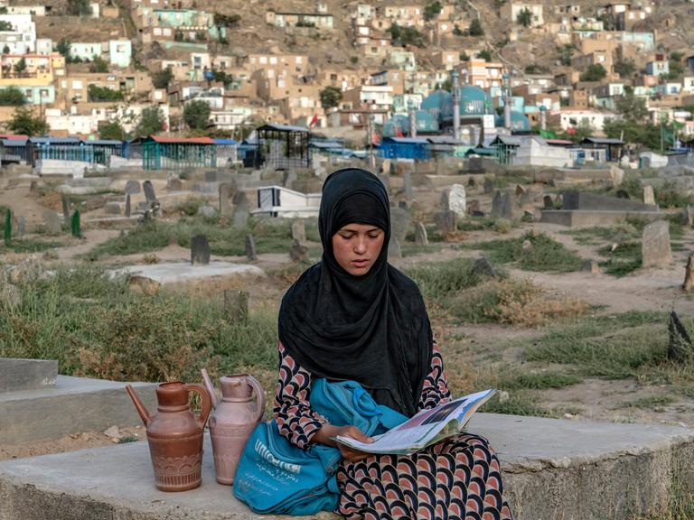 Eine 14-jährige Wasserverkäuferin auf einem Kabuler Friedhof, lesend, während sie auf Kundschaft wartet