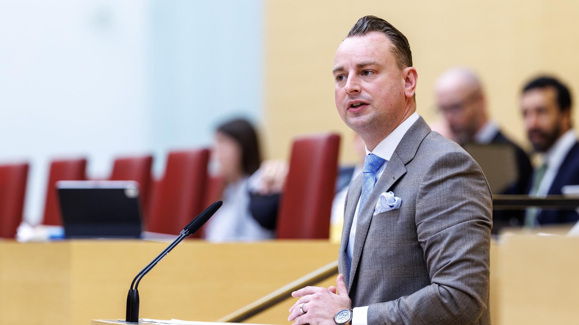 Benjamin Nolte von der AfD spricht an einem Rednerpult. Er trägt einen dunkelbraunen Anzug und eine blaue Krawatte.