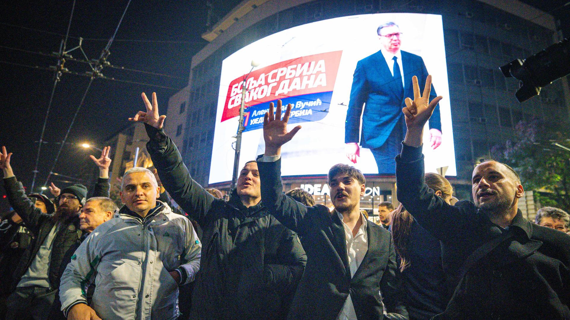 Menschen jubeln vor einem großen Bildschirm, der Aleksandar Vucic zeigt.