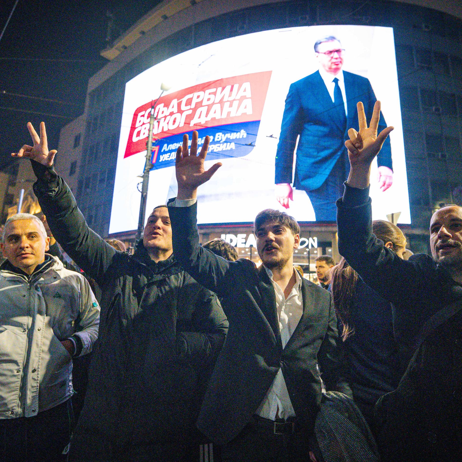 Menschen jubeln vor einem großen Bildschirm, der Aleksandar Vucic zeigt.