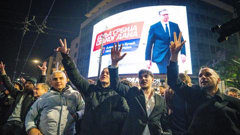 Menschen jubeln vor einem großen Bildschirm, der Aleksandar Vucic zeigt.