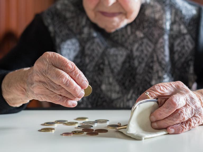 Eine ältere Frau, deren Gesicht durch Anschnitt und Unschärfe nicht erkenntlich ist, sitzt am Tisch und zählt mit faltigen Händen die Münzen aus Ihrer Geldbörse. (Symbolfoto)