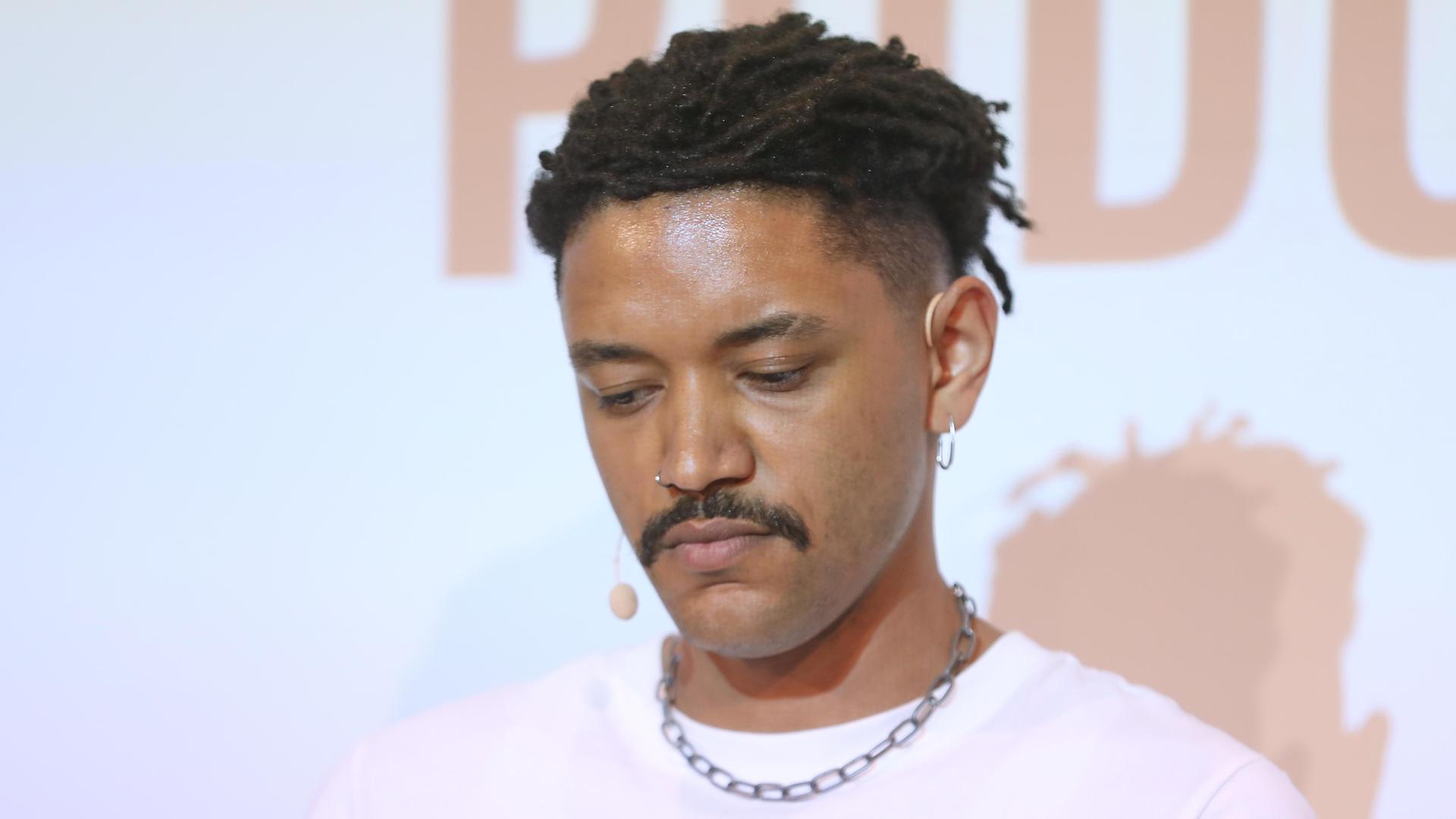 Der Journalist Don Pablo Mulemba blickt nach unten. Er trägt einen Schnurrbart und hat dunkle Haare, ein rosa T-Shirt mit einer Kette. Der Journalist Don Pablo Mulemba blickt nach unten. Er trägt einen Schnurrbart und hat dunkle Haare, ein rosa T-Shirt mit einer Kette.