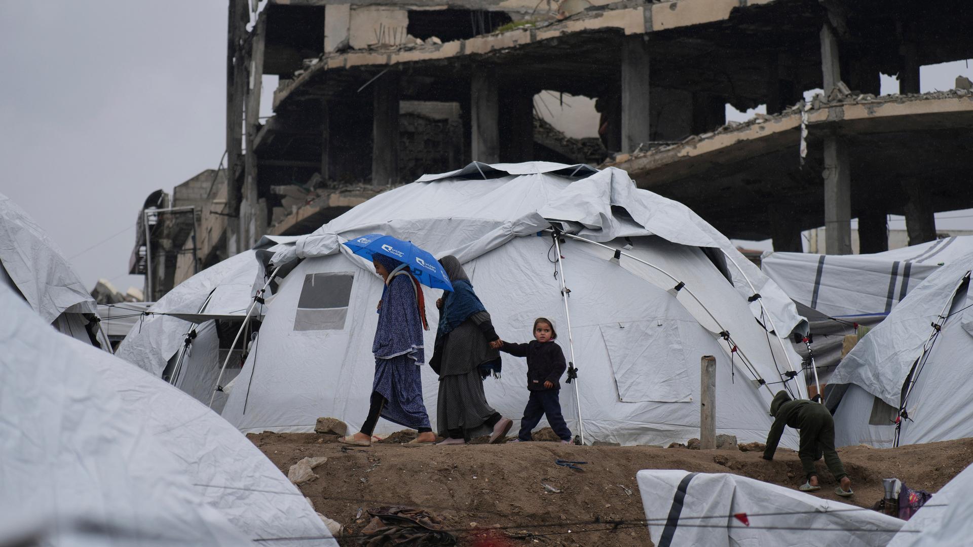 Eine palästinensiche Familie geht zwischen Zelten vor zerstörten Häusern in Gaza-Stadt umher.