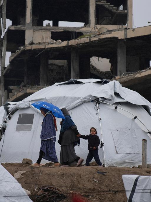 Eine palästinensiche Familie geht zwischen Zelten vor zerstörten Häusern in Gaza-Stadt umher.