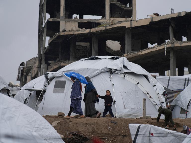 Eine palästinensiche Familie geht zwischen Zelten vor zerstörten Häusern in Gaza-Stadt umher.