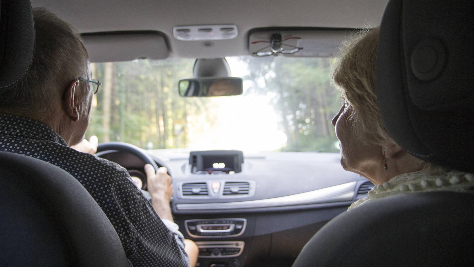 Ein älteres Ehepaar fährt im Auto. Man sieht sie vom Rücksitz aus.