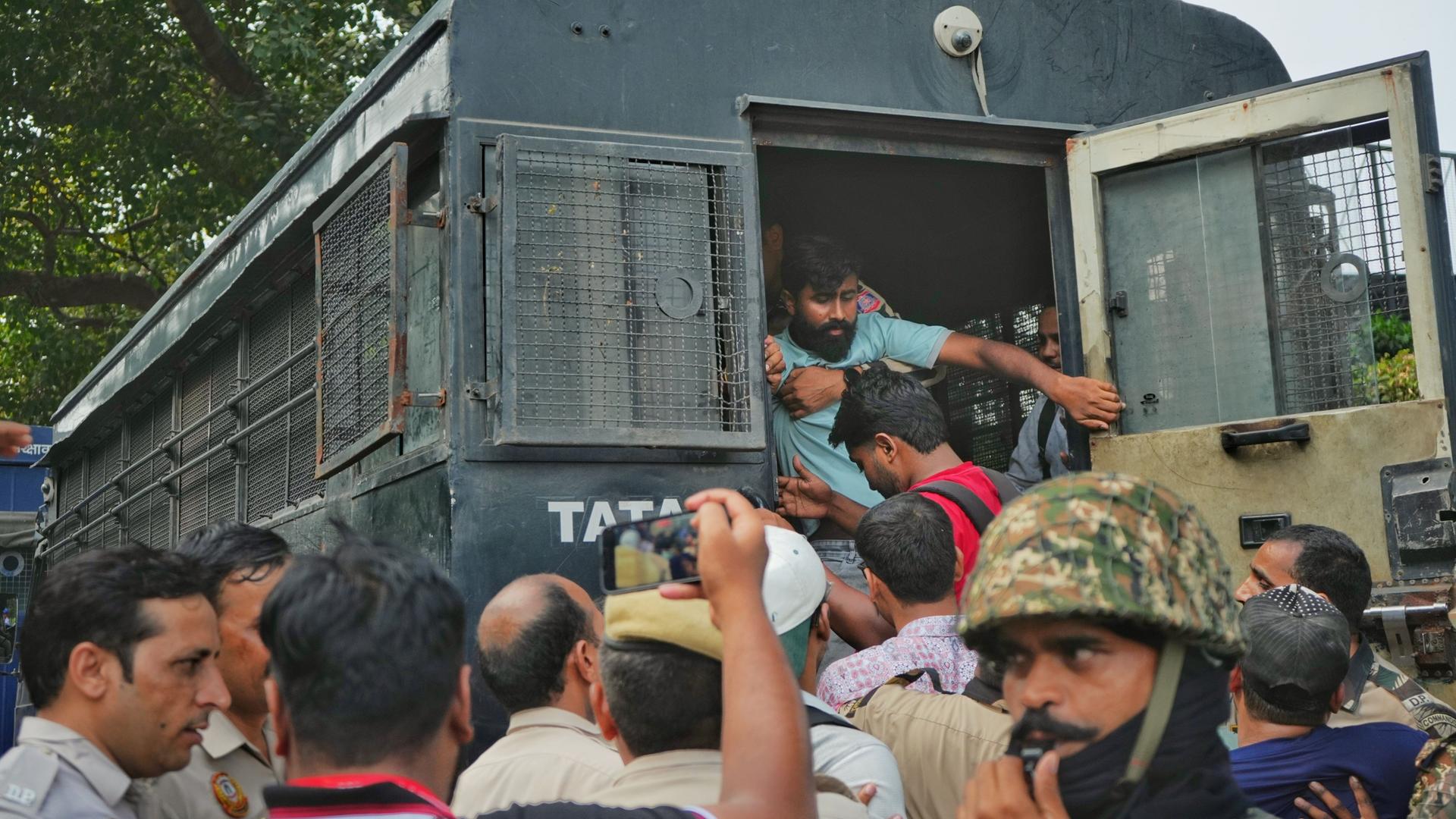 Eine Menschenmenge vor einem vergitterten Fahrzeug in Neu-Delhi, in das gerade ein Mann hineingezerrt wird. 