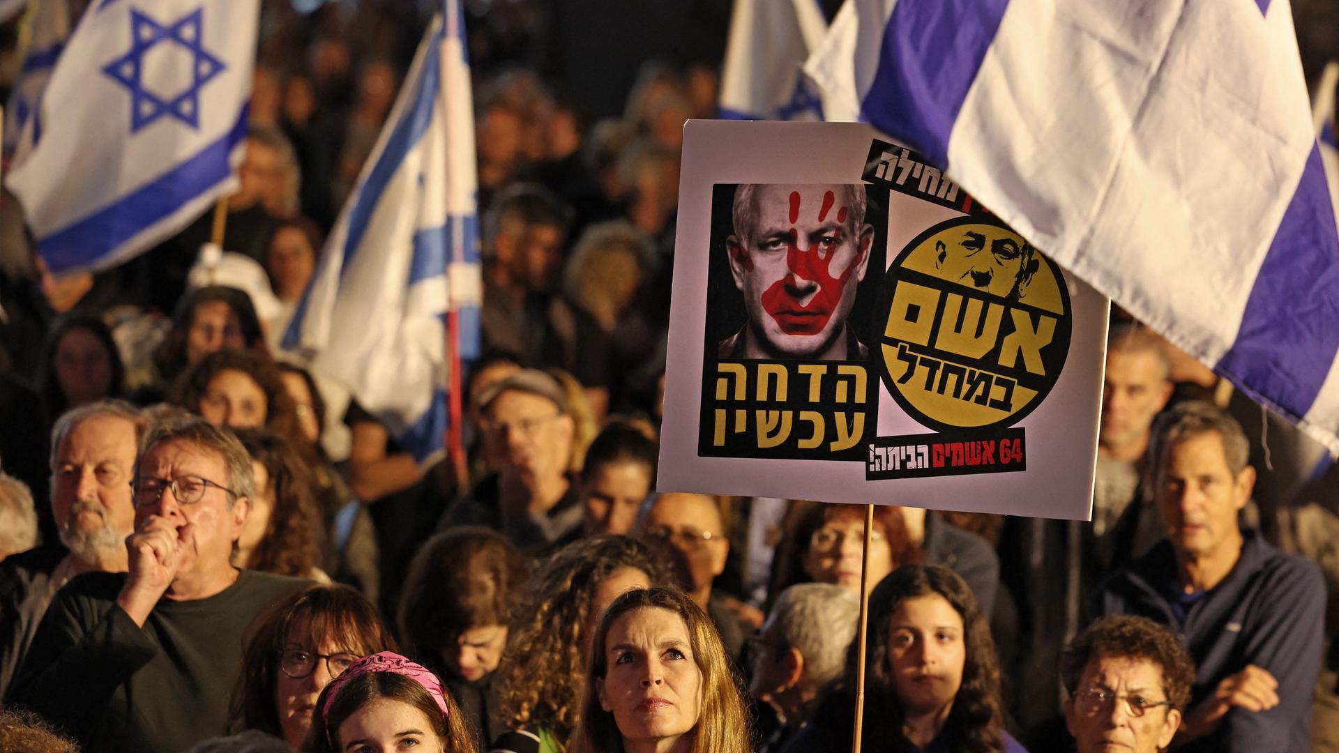 Teilnehmer an einer Anti-Regierungs-Demonstration halten in der israelischen Großstadt Tel Aviv Landesflaggen und politische Botschaften in die Höhe.