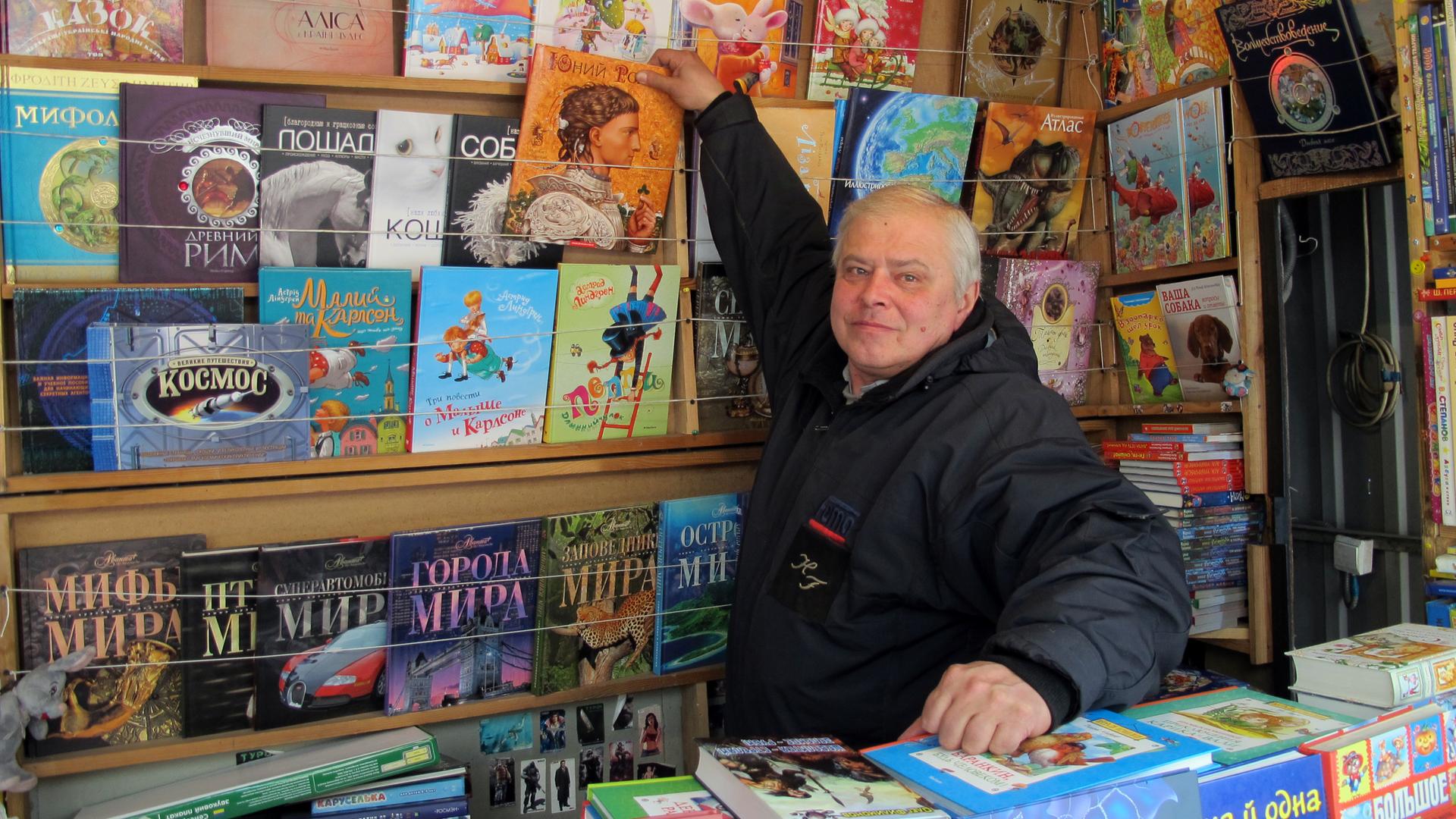 Ein älterer Mann steht in seinem Bücherstand und zeigt eines seiner Kinderbücher.