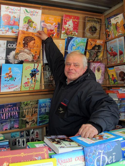 Ein älterer Mann steht in seinem Bücherstand und zeigt eines seiner Kinderbücher.