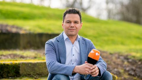 Ein Mann mit braunem Haar und blauem Anzug hält ein ZDF-Mikro in der Hand und blickt in die Kamera.
