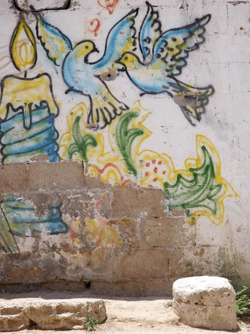 Ein Mitglied der Al-Qassam Brigade zielt mit einem Gewehr an einer Mauer in Gaza Stadt. Auf der Mauer ist ein Graffiti mit bunten Tauben als Symbol für Frieden zu sehen. Ein Mitglied der Al-Qassam Brigade zielt mit einem Gewehr an einer Mauer in Gaza Stadt. Auf der Mauer ist ein Graffiti mit bunten Tauben als Symbol für Frieden zu sehen.
