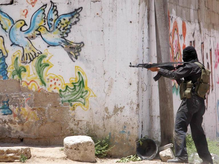 Ein Mitglied der Al-Qassam Brigade zielt mit einem Gewehr an einer Mauer in Gaza Stadt. Auf der Mauer ist ein Graffiti mit bunten Tauben als Symbol für Frieden zu sehen. Ein Mitglied der Al-Qassam Brigade zielt mit einem Gewehr an einer Mauer in Gaza Stadt. Auf der Mauer ist ein Graffiti mit bunten Tauben als Symbol für Frieden zu sehen.