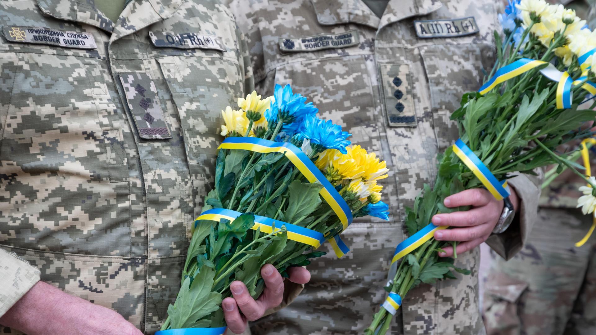 Ukrainische Soldaten halten blau-gelbe Blumensträuße in den Händen Ukrainische Soldaten halten blau-gelbe Blumensträuße in den Händen