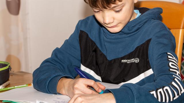 Ein Kind macht Hausaufgaben und schreibt in ein Heft.