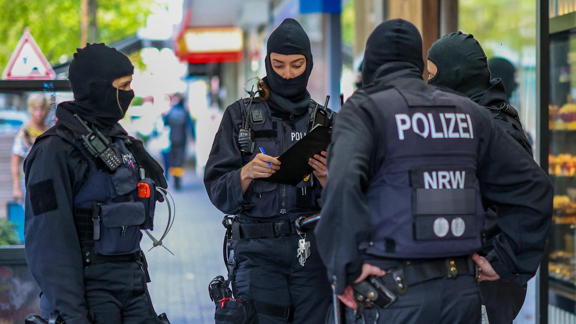 Razzia gegen Geldwäsche bei den Hells Angels: Mehrere schwarz gekleidete bewaffnete Polizisten mit schusssicheren Westen und Sturmhauben stehen in Duisburg vor einem Gebäude. 