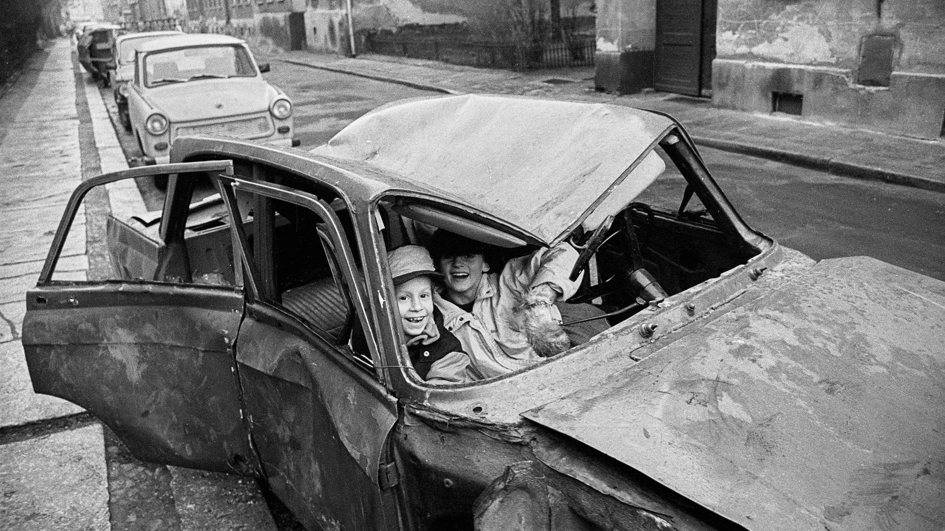 Lachende Kinder sitzen in einem Autowrack in der Steinstraße, Berlin 1990.